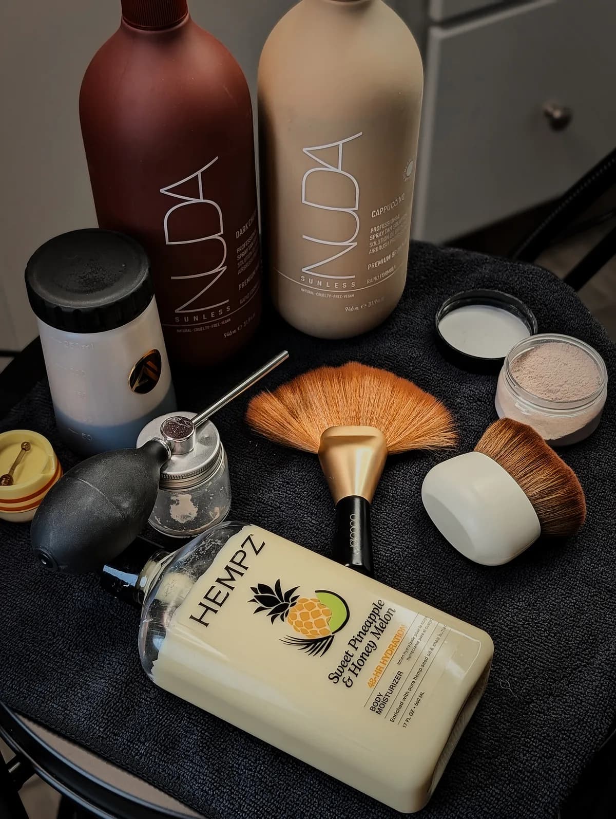 Glowtoure professional spray tan kit — salon-grade Nuda sunless solutions, airbrush, and application brushes on the studio cart